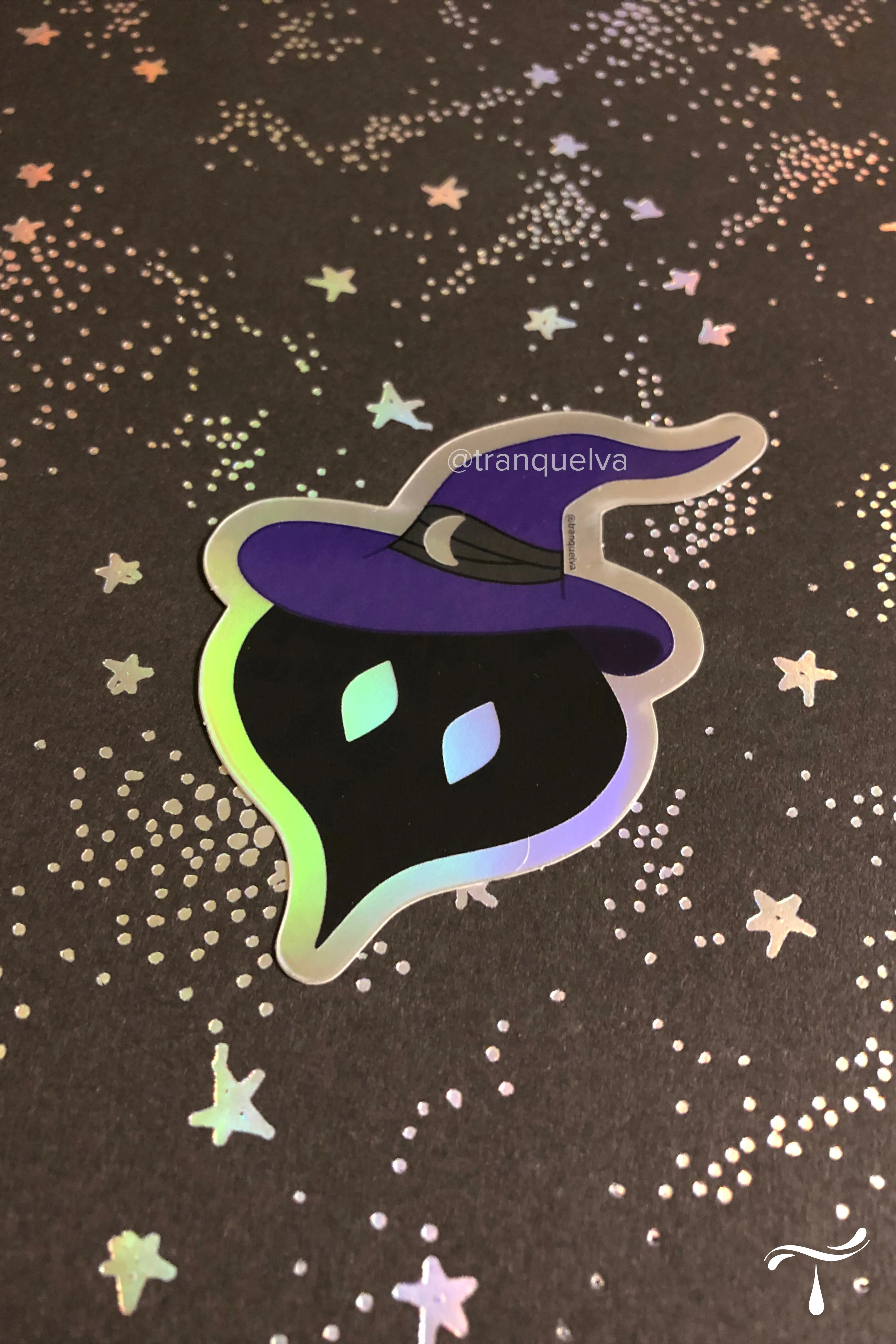 Holographic sticker of a black ghost wearing a purple witch hat, on dark paper with iridescent stars
