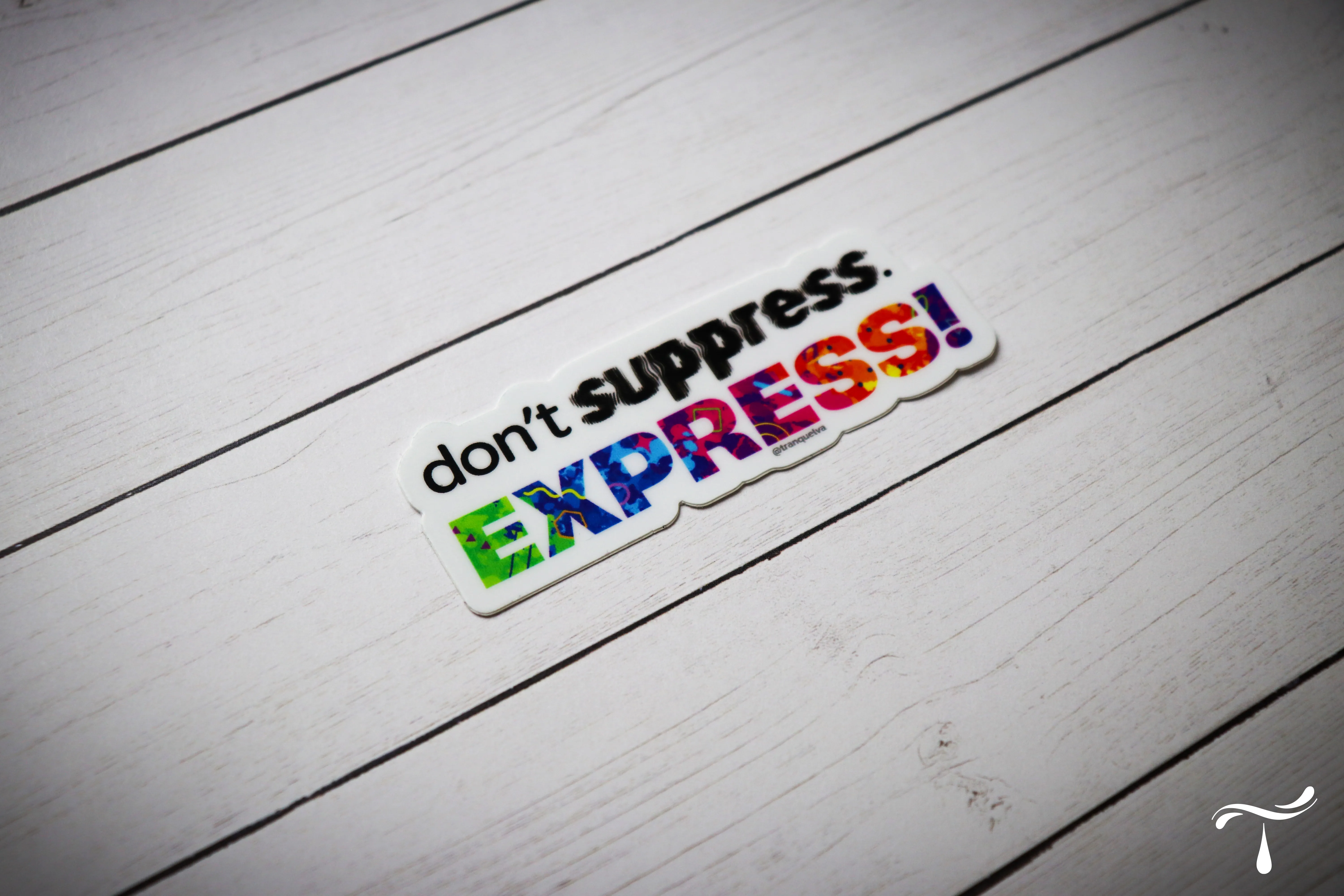 Sticker reading "don't suppress. EXPRESS!" with the word express filled in colourful patterns, on white wood